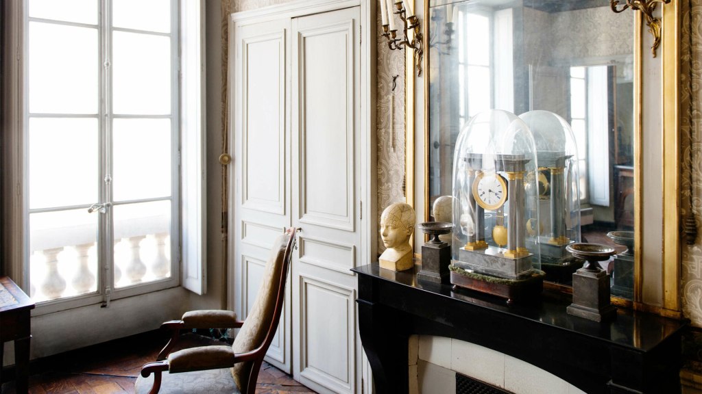 Interior shot of museum drawing room, focused on a gold clock, mirror and phrenology bust on a mantlepiece.