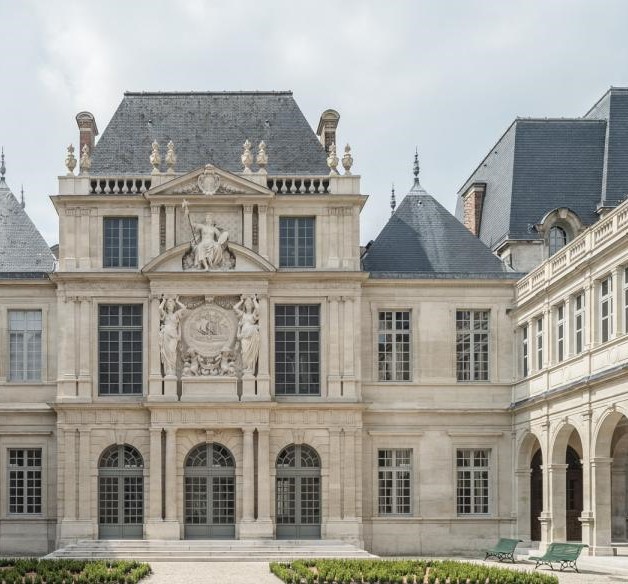 Stone facade of three-storey Parisian mansion with many windows and an open courtyard